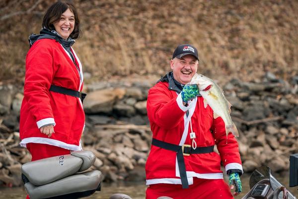 Couple in Santa outfits smiling while one holds a fish he just caught